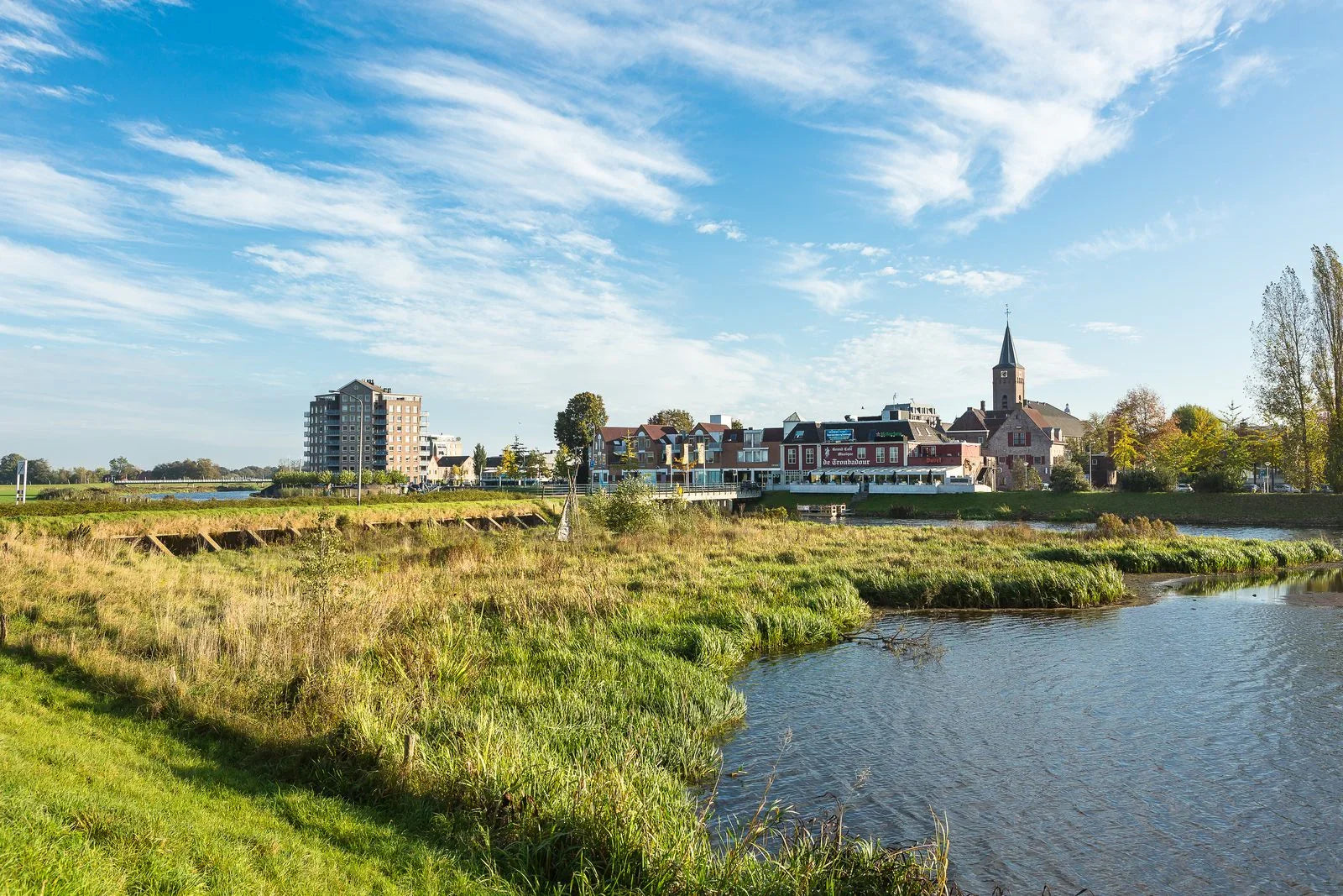 Rivierlandschap met een klein dorp, kerk met toren en moderne gebouwen onder een blauwe hemel