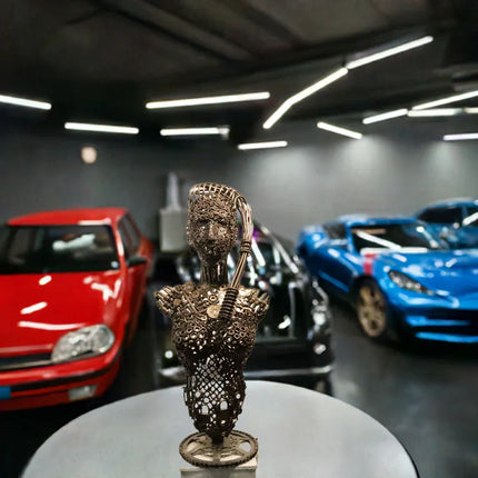Sculptuur van mechanische vrouw gemaakt van metalen onderdelen in garage met rode, zwarte en blauwe auto
