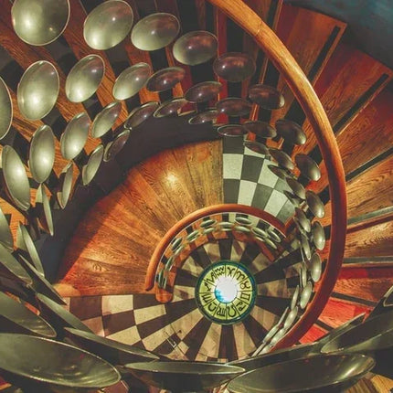 Spiraalvormige houten trap met zwart-witte tegels en metalen decoratieve schijven aan leuning